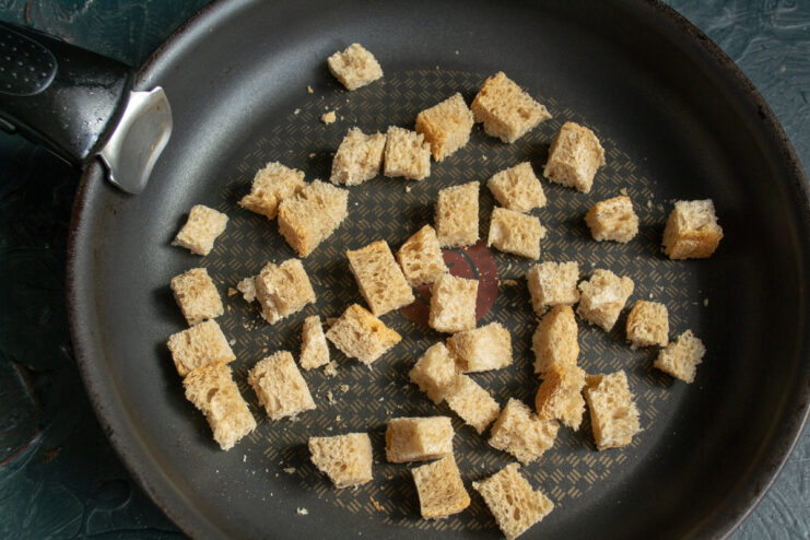 Toasting bread cubes in a skillet until they turn a golden brown color