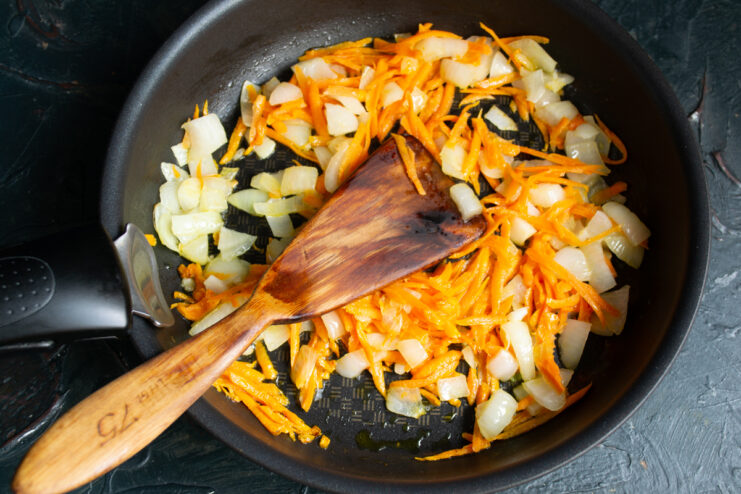 Sautéing the vegetables Sautéing chopped onions and grated carrots in a hot skillet.