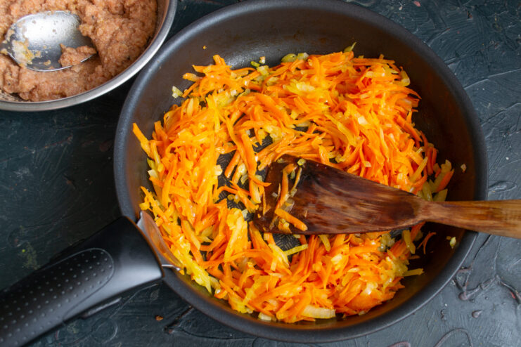 Sautéing grated carrots and chopped onions in a skillet