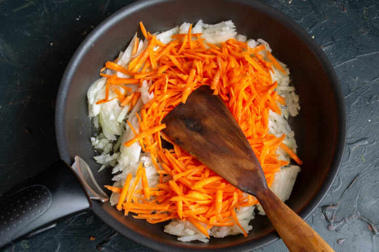 Sautéing the vegetables Sautéing grated carrots and chopped onions in a skillet.