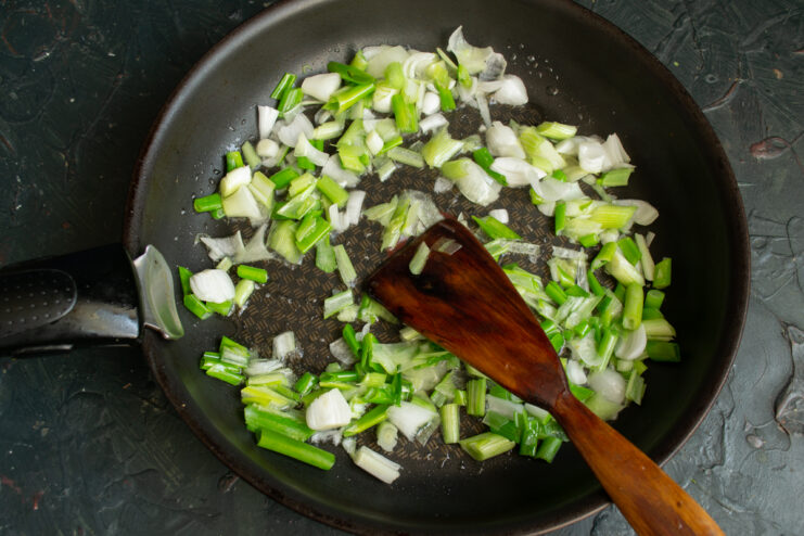 Preparing the topping Sautéing chopped green onions in a skillet