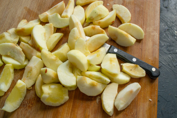 Peeled and sliced apples on a wooden cutting board.
