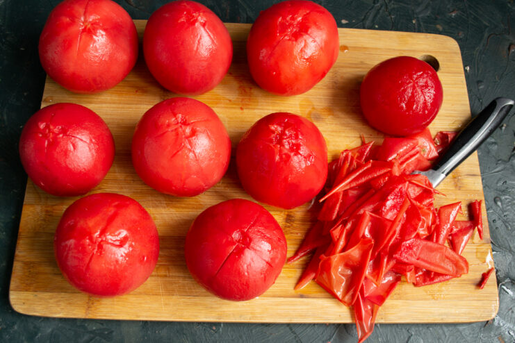 Peeling the blanched tomatoes Peeled fresh tomatoes resting on a wooden cutting board
