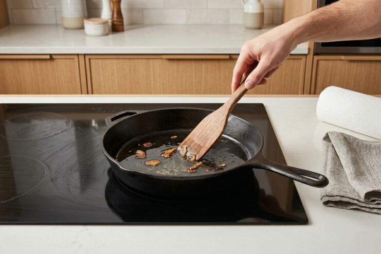 Removing Food Residue Scraping burnt food remnants from a cast-iron skillet using a wooden spatula.