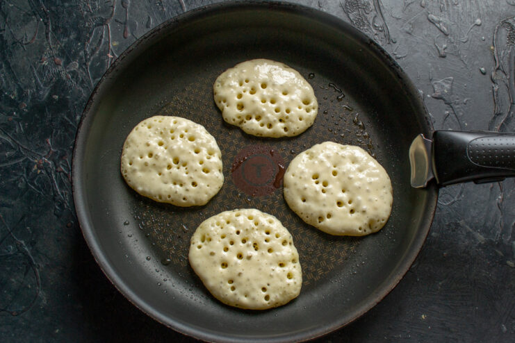 Pancakes frying in a skillet showing bubbles on the surface