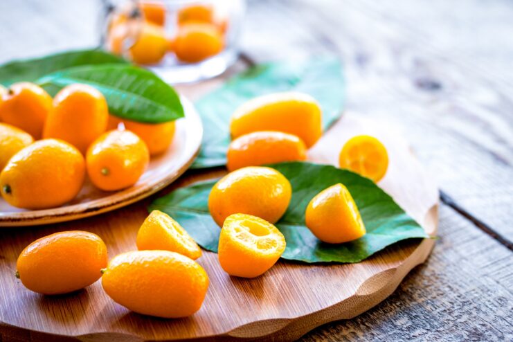 Fresh Kumquat Fruits Small orange kumquats with green leaves arranged on a wooden board