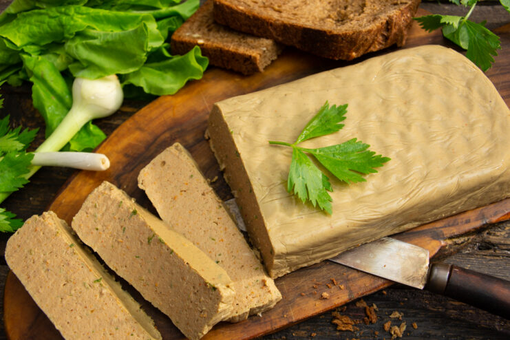 Sliced chicken liver pâté with gelatin served on a wooden board with fresh herbs and bread.