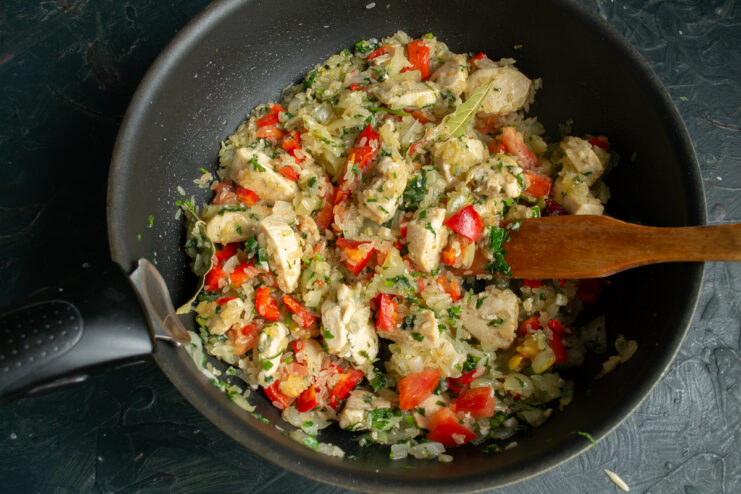 Stirring rice with vegetables and chicken in a pan before adding broth