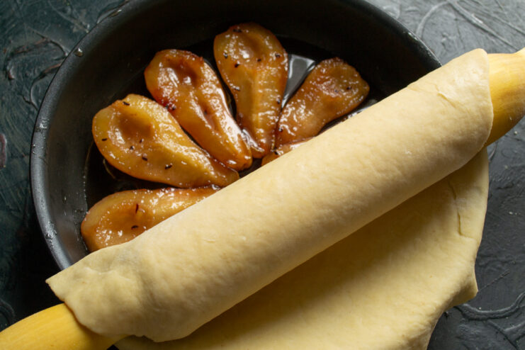 Assembling the Tart Transferring rolled dough draped over a rolling pin onto a skillet with pears