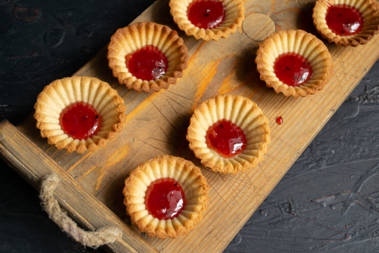 Adding the jam Shortcrust pastry shells filled with a spoonful of strawberry jam