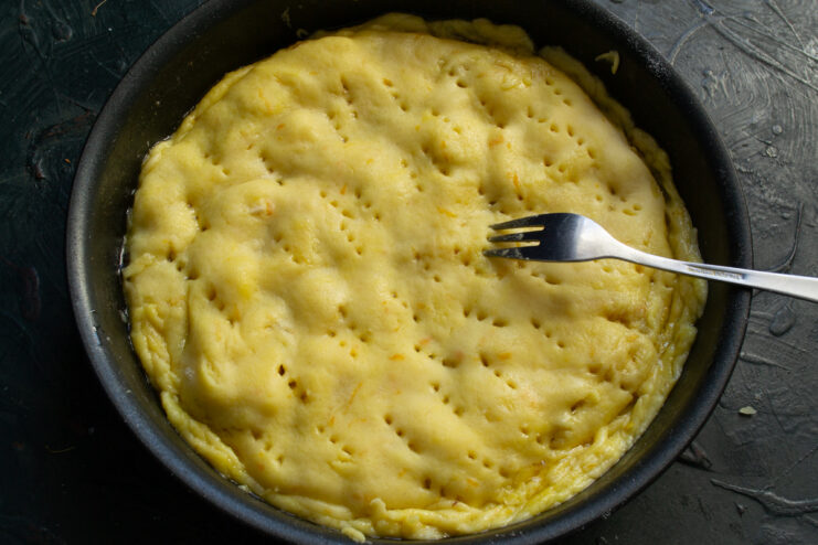 Tart covered with dough in a skillet, with fork holes on the surface.