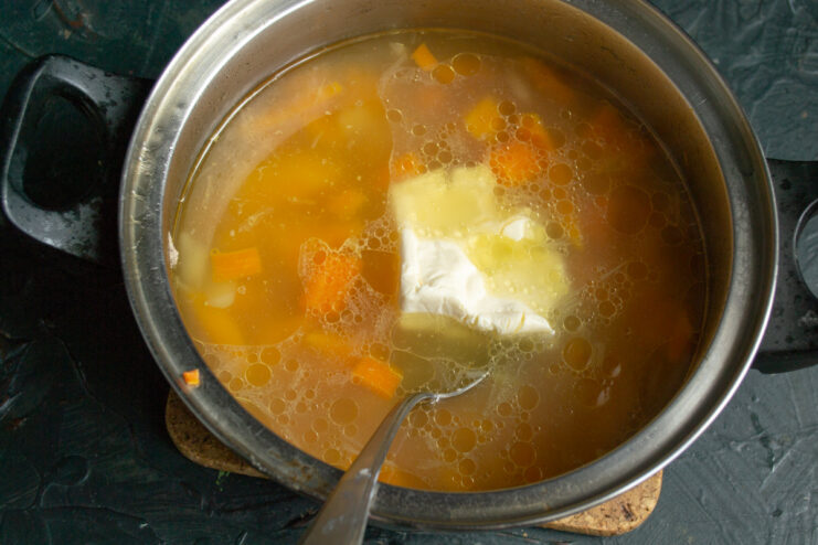 Crumbled processed cheese being added to the pot with boiled vegetables