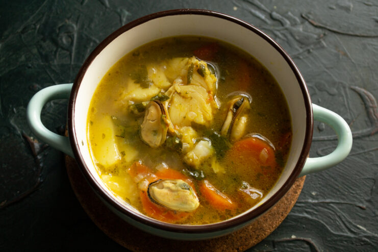 Serving the fish soup Ladle pouring hot cod and mussel soup into a deep serving bowl
