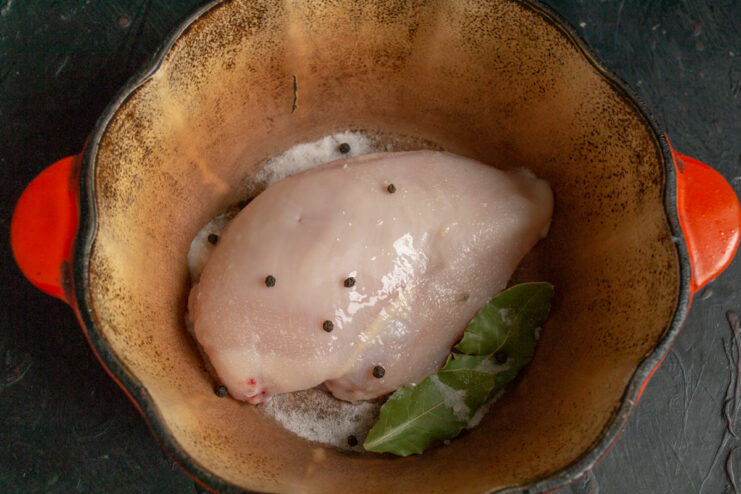 Preparing the chicken fillet Raw chicken fillet in a pot with salt, bay leaf, and black peppercorns