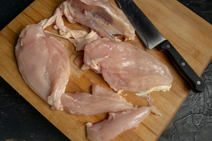 Separating chicken meat from the bone Cutting chicken breast fillet from the bone on a cutting board
