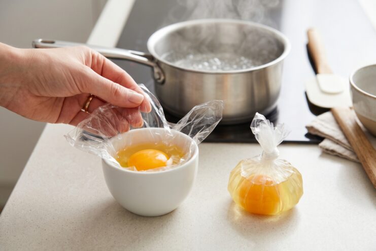 Poached Egg in Plastic Wrap Raw egg tightly secured inside a small pouch made of plastic wrap, ready for the simmering water bath.