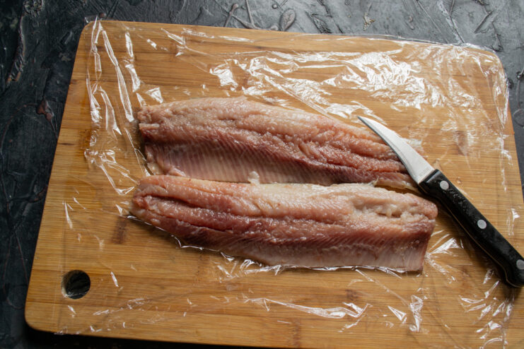 Prepared boneless herring fillets arranged back-to-back on plastic wrap.