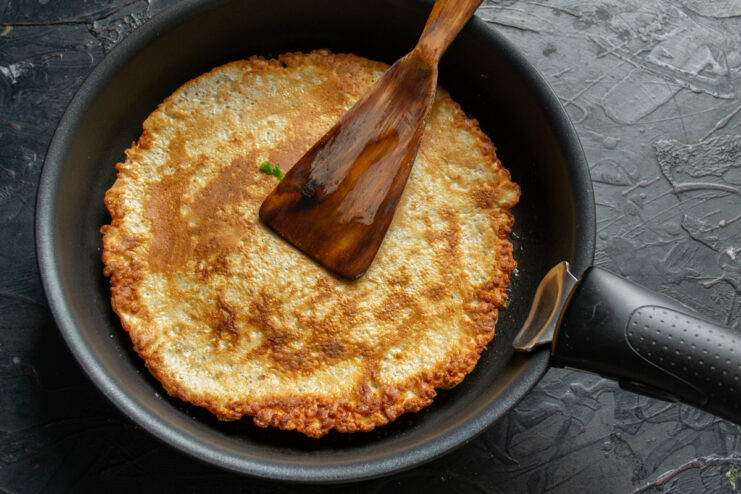 Frying Until Golden Brown Flipping a golden-brown cooked oat pancake in a hot skillet using a wooden spatula