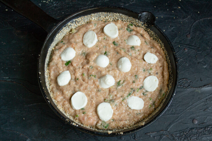 Adding the cheese layer Halved mozzarella balls arranged on top of the raw fish casserole.