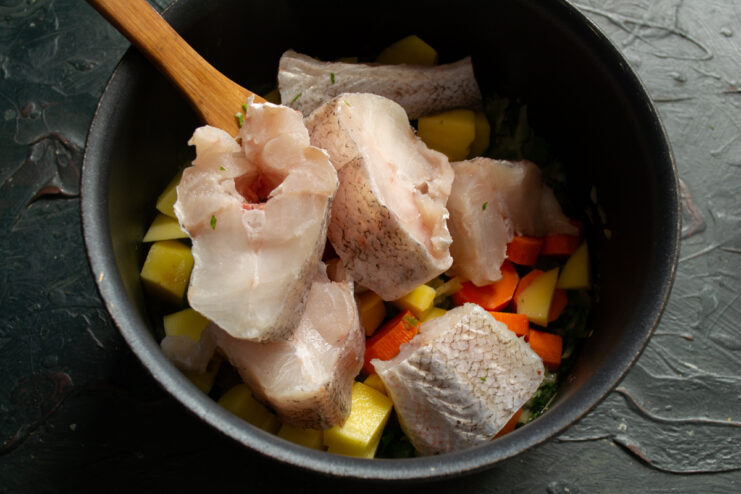 Adding the fish Portioned cuts of fresh cod layered directly over chopped vegetables in a pot