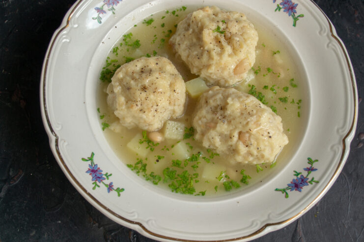 Serving the finished dish Ladle pouring chicken soup with bean dumplings into a ceramic bowl
