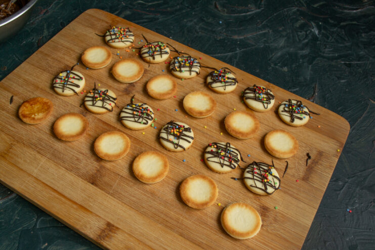 Adding Sprinkles Scattering colorful candy sprinkles over wet chocolate drizzle on cookies