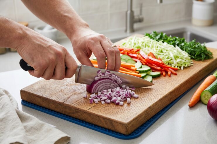 Safe Knife Handling Techniques Chef demonstrating the claw grip technique while slicing a red onion on a wooden cutting board.