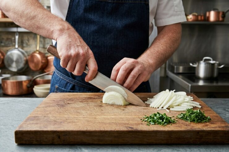 Professional chef dicing an onion with a large chef's knife on a wooden board