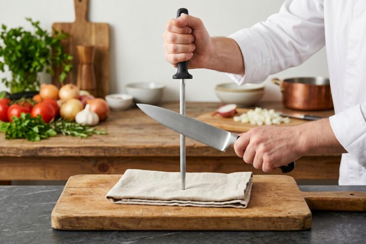 Cook sliding a kitchen knife down a vertical steel honing rod