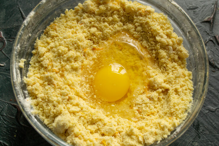 Process of making dough with flour, butter, and an egg in a glass bowl.