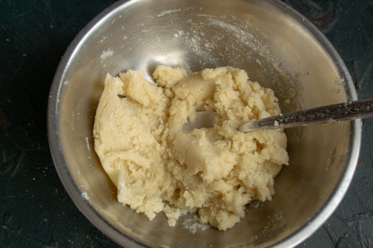 Hands kneading thick marzipan dough inside a mixing bowl