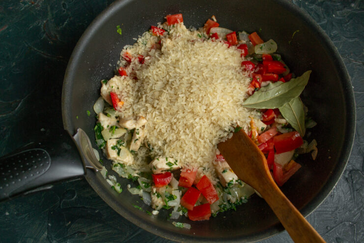 Pouring parboiled rice into the skillet with chicken and vegetables