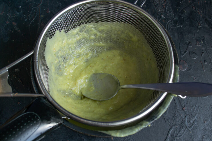 Pushing the green bean soup through a fine metal mesh sieve