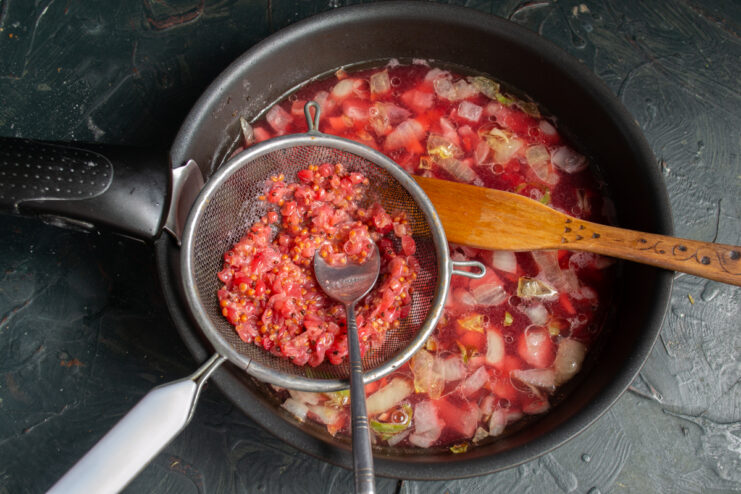 Pressing the boiled redcurrant mash through a fine-mesh sieve with a spoon