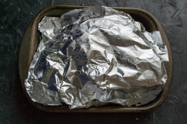Baking peppers under foil Baking sheet of stuffed bell peppers covered with aluminum foil