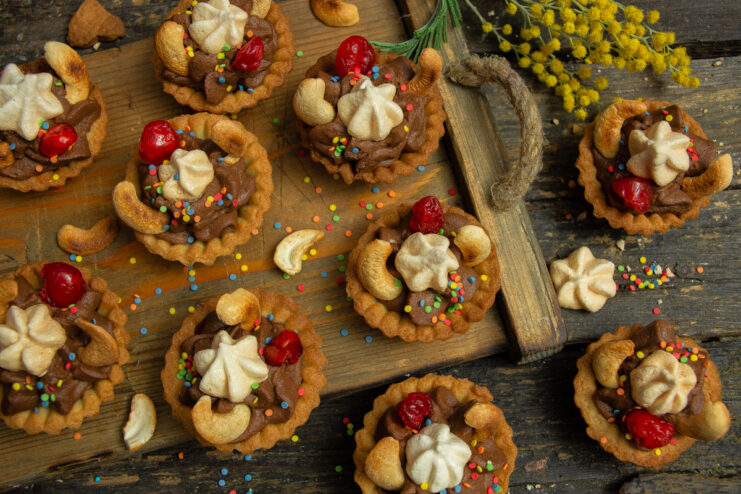 Finished petits fours with chocolate mousse, meringues, and cherries on a wooden background