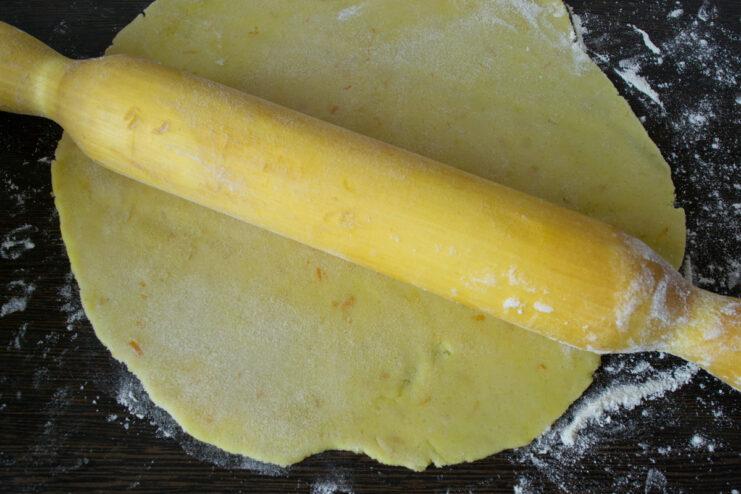 Rolled out sheet of shortcrust pastry on a dark table under a rolling pin.
