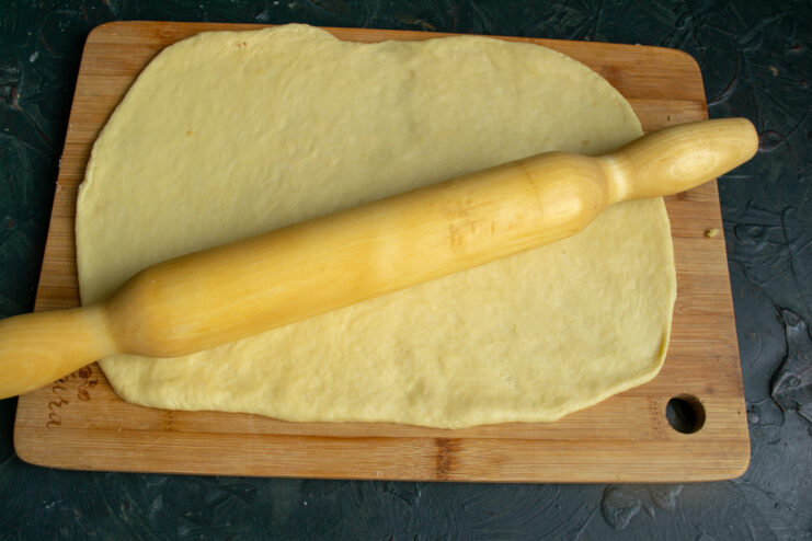 Rolling the Dough Rolled sheet of dough on a wooden board with a rolling pin