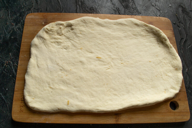 Rolling out the dough rectangle Rolling out the smooth yeast dough into a large rectangle on a wooden cutting board