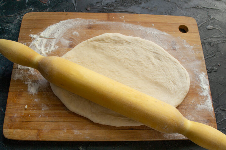 Rolling out dough with a wooden rolling pin to a one centimeter thickness