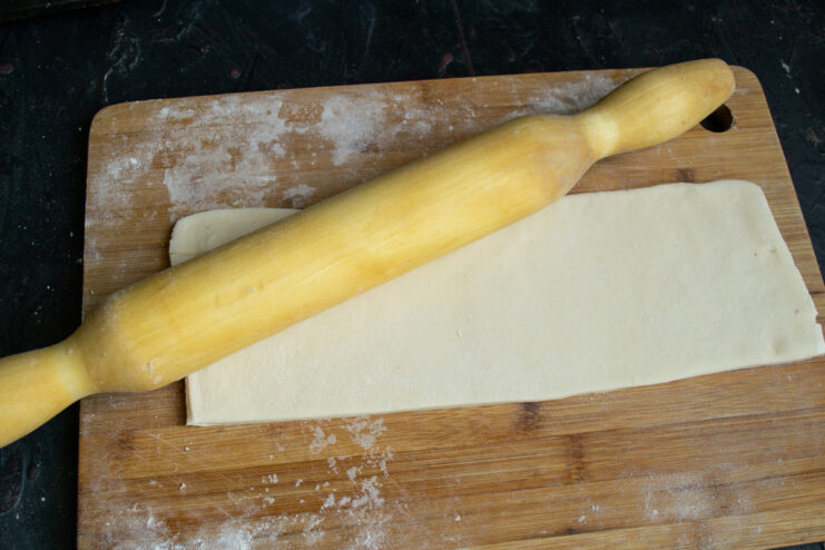 Rolling out pastry dough with a rolling pin on a wooden board