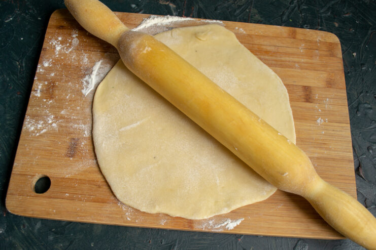 Rolling out the dough Rolling out the pastry dough with a rolling pin on a wooden board
