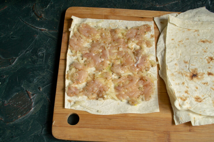 Spreading a thin layer of seasoned ground meat evenly over the lavash