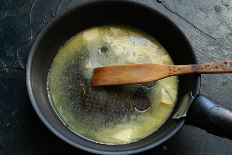 Melted butter in a black skillet with a wooden spatula.