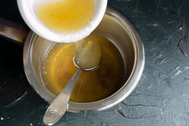 Making the jelly base Stirring bloomed gelatin into a saucepan of hot, strained chicken broth.