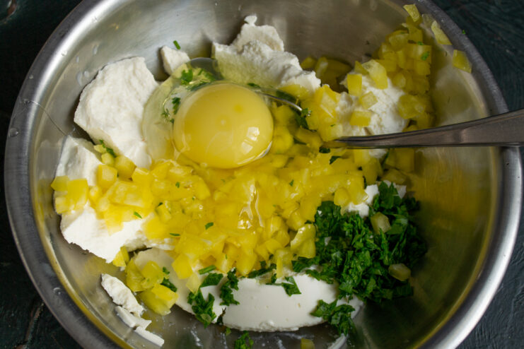 A cracked egg in a mixing bowl with fritter ingredients