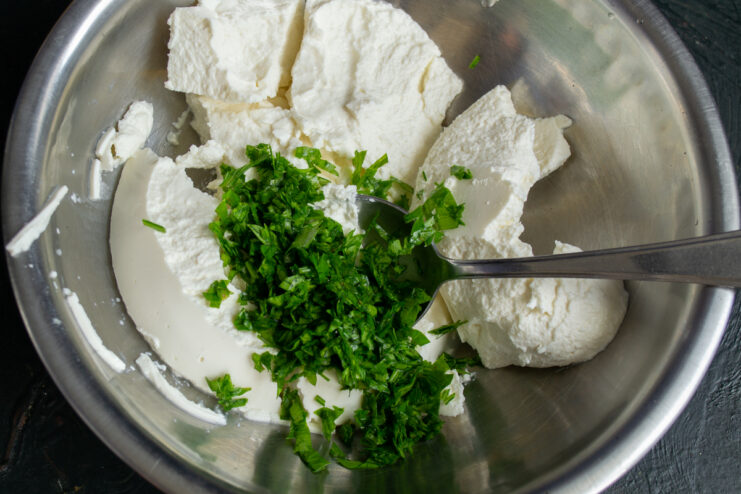 Ricotta cheese and finely chopped parsley in a metal mixing bowl