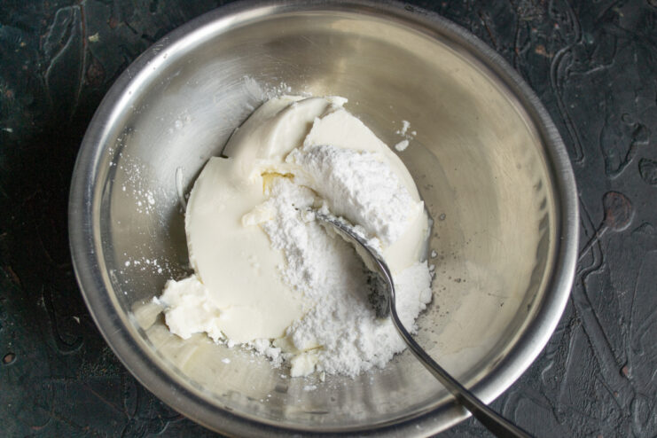 Mixing ricotta cheese with powdered sugar in a metal bowl.