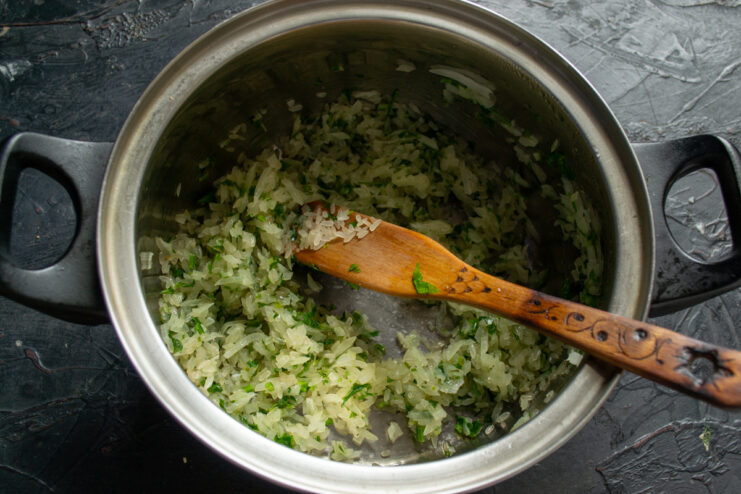 Toasting the rice Stirring raw rice into the pot with sautéed onions and fresh herbs
