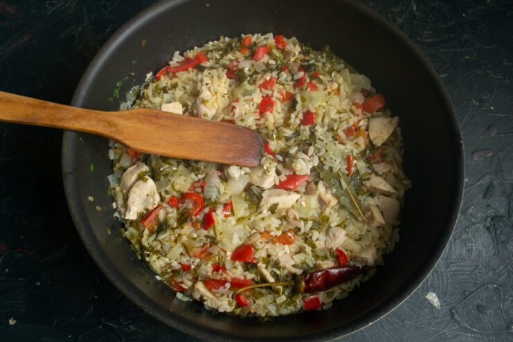Rice, chicken, and vegetables simmering in broth covered with a lid